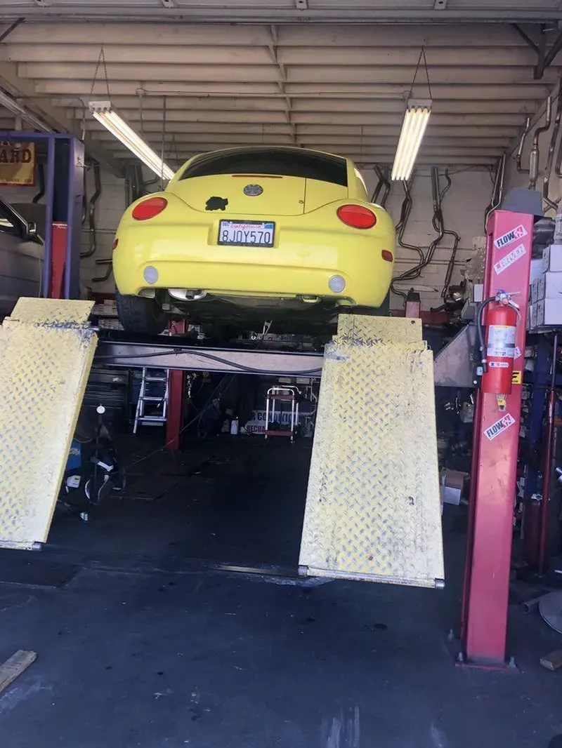 Yellow car on a hydraulic lift in a garage, two ramps, red supports, fluorescent lighting.
