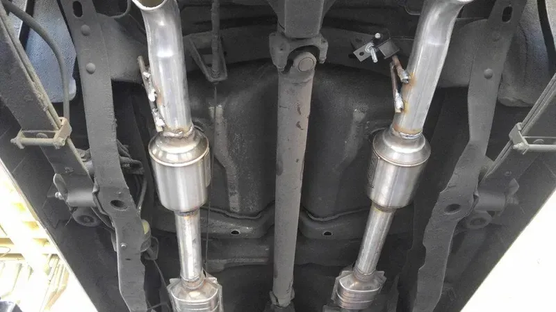Undercarriage of a vehicle showing dual exhaust pipes, catalytic converters, and drive shaft.