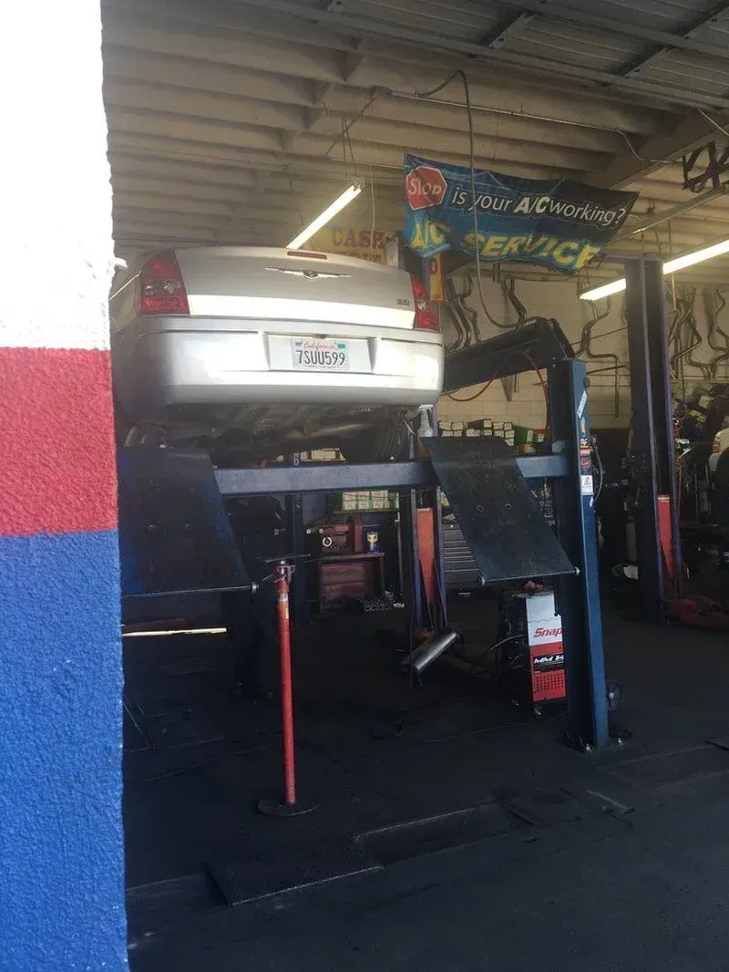 Silver car elevated on a hydraulic lift inside an auto repair shop.
