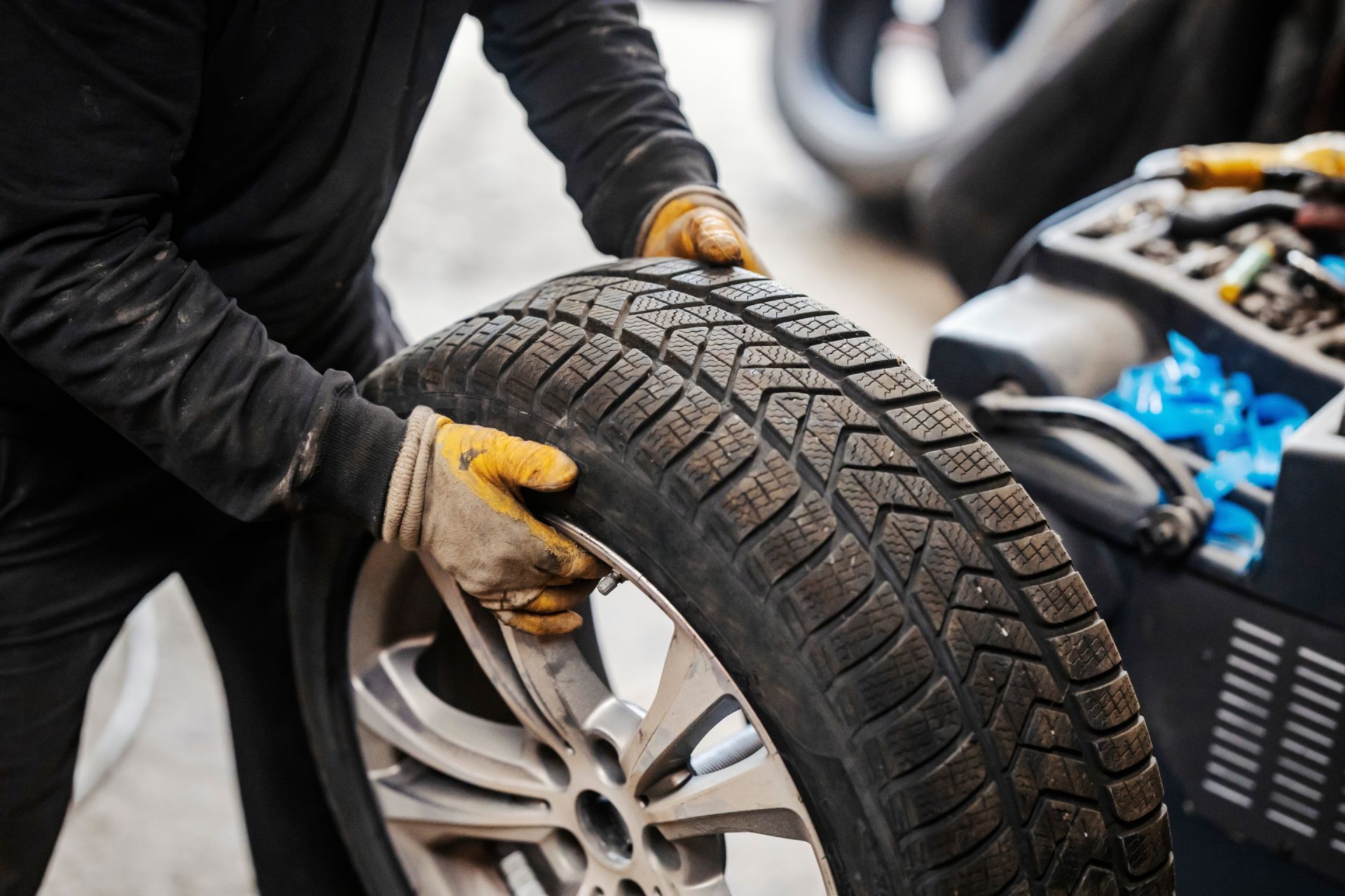 Mechanic in work clothes holding a tire with a silver rim, working in a tire shop.