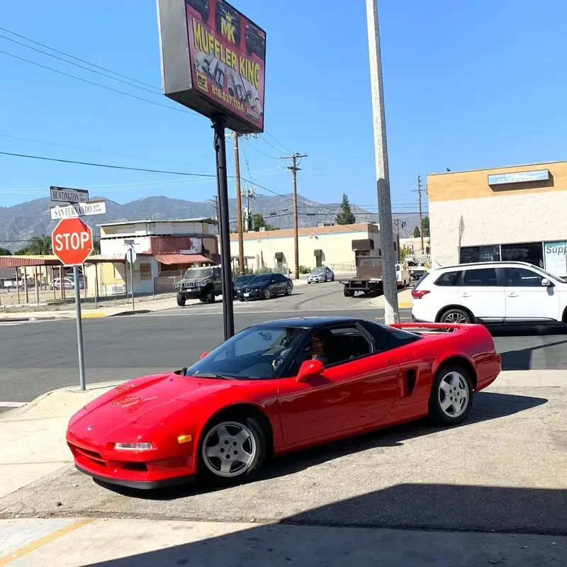Red Honda NSX sports car parked on a street corner under a sunny sky.