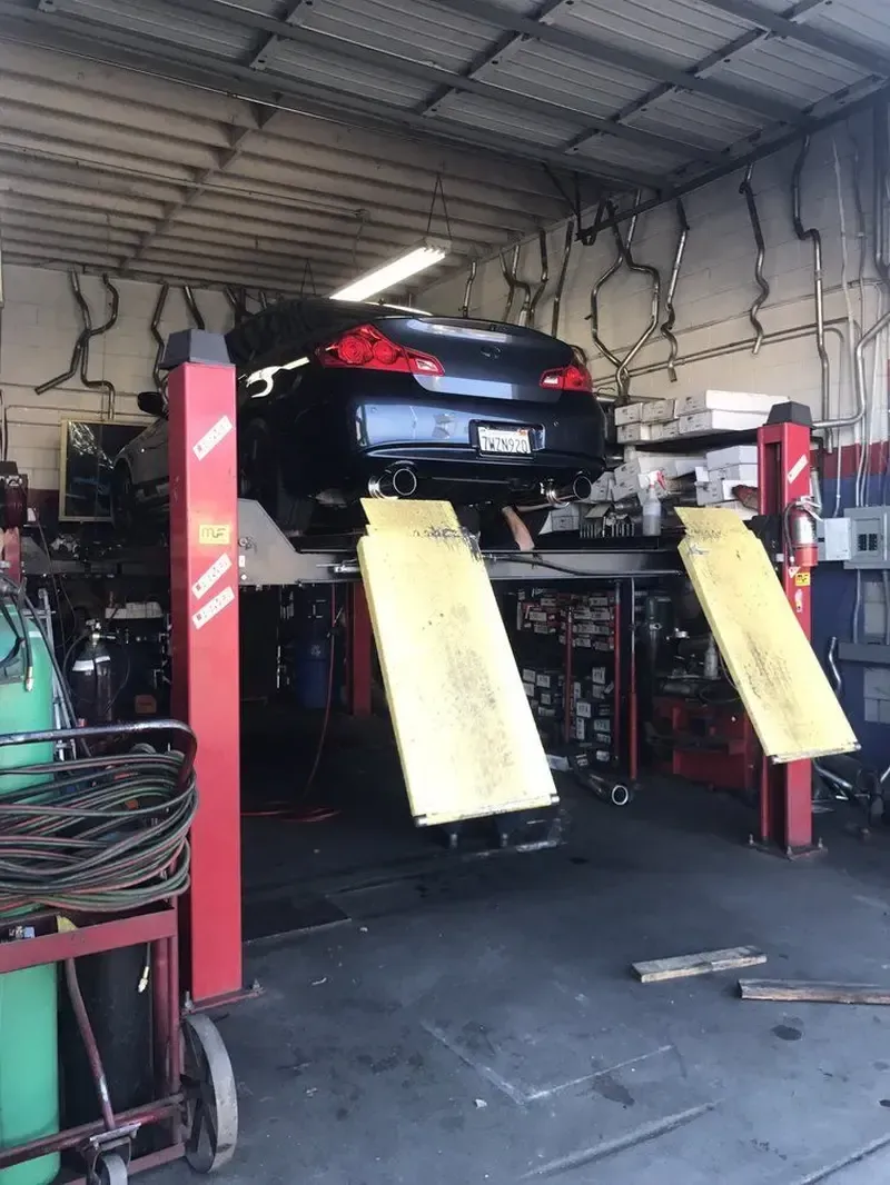 A black car raised on a lift inside a car repair shop.