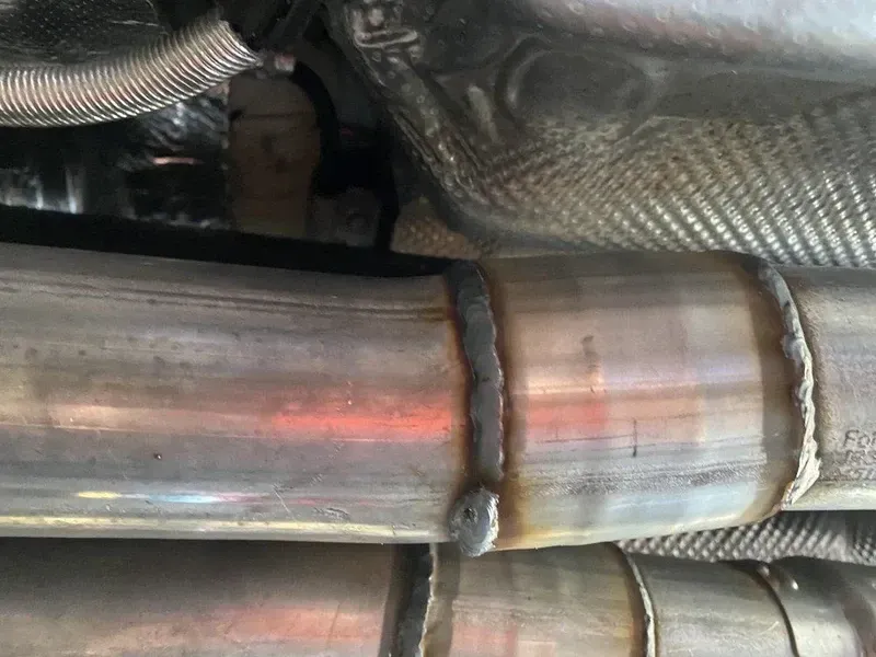 Close-up of welded exhaust pipes under a car, with heat shielding visible.