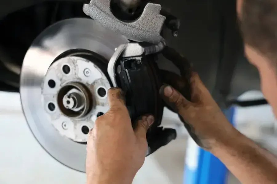Hands of a mechanic replacing brake pads on a car's disc brake rotor.