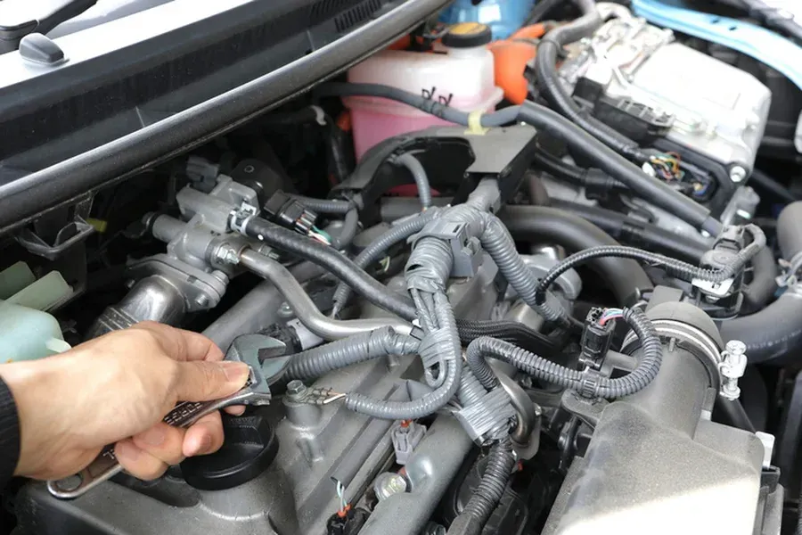 Hand using a wrench to work on a car engine, highlighting engine components and hoses.