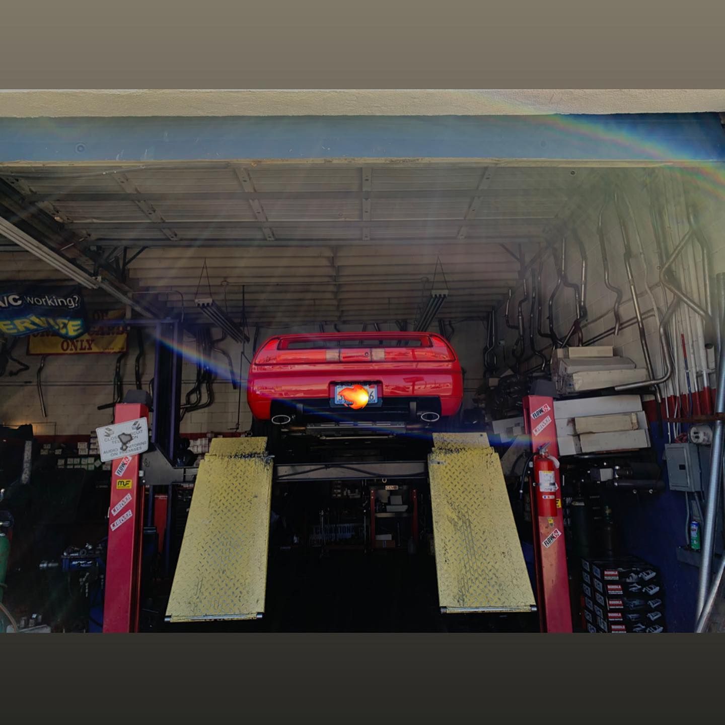 Red sports car on a lift in a garage, under a metal beam.