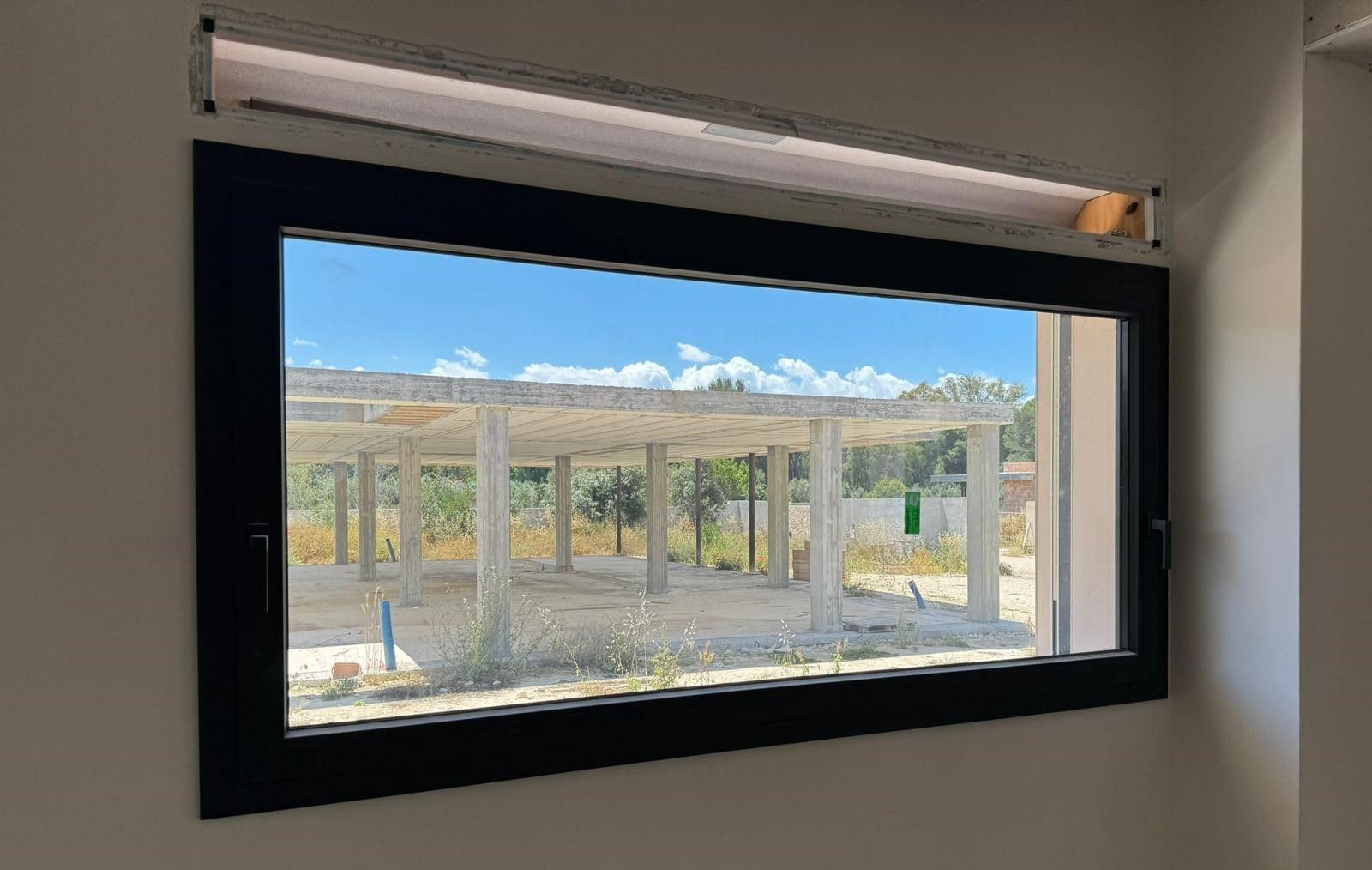 Finestra con cornice nera che mostra un cantiere edile sotto un cielo azzurro brillante; 