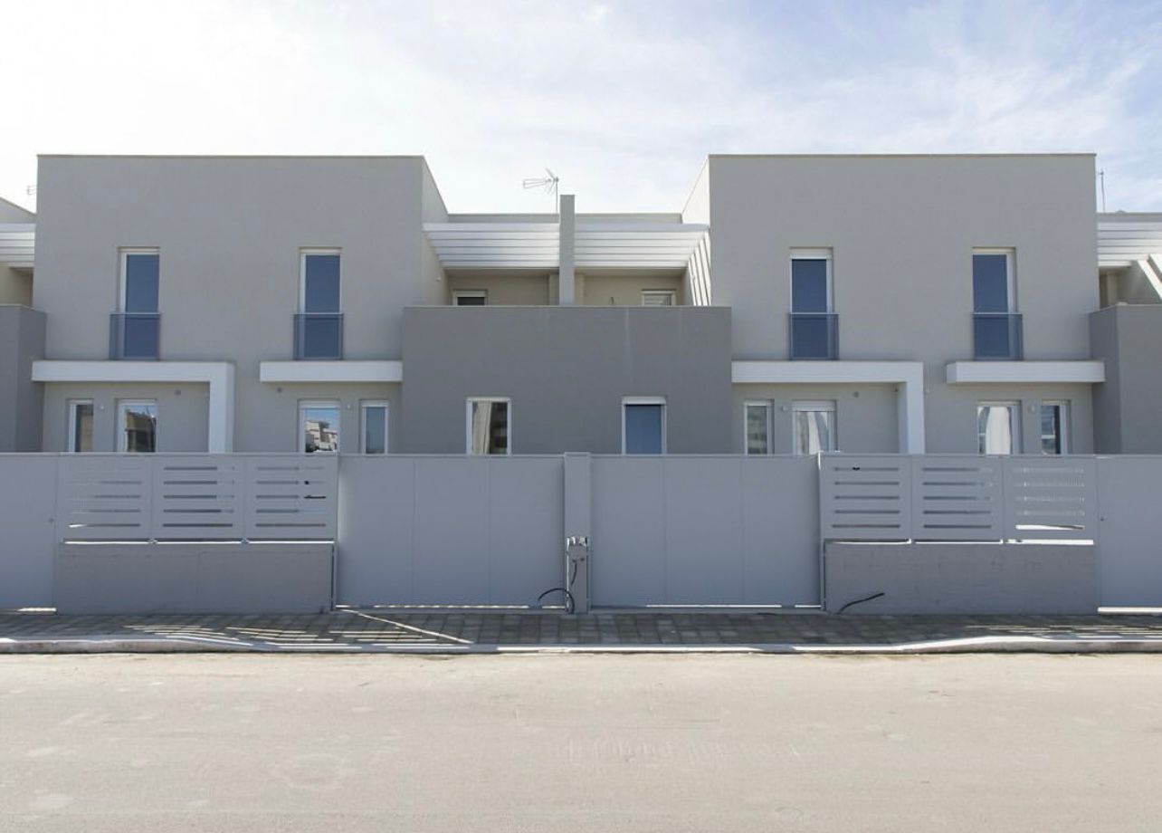 Case a schiera grigie dietro una recinzione coordinata e una strada asfaltata.