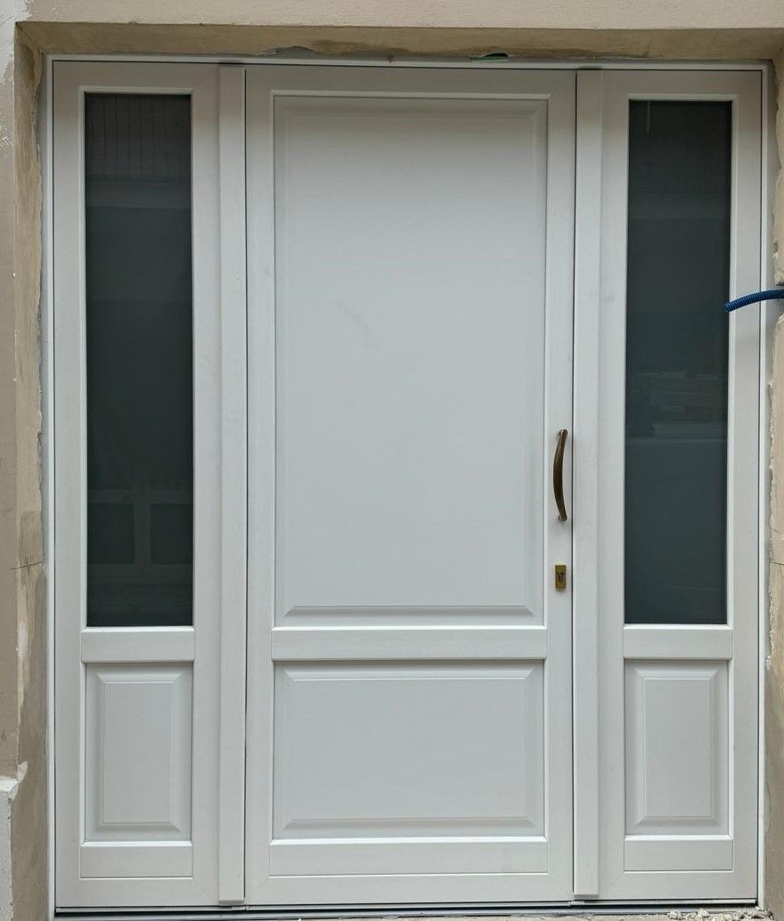 Porta d'ingresso bianca con finestre laterali; sono visibili la maniglia e la serratura.