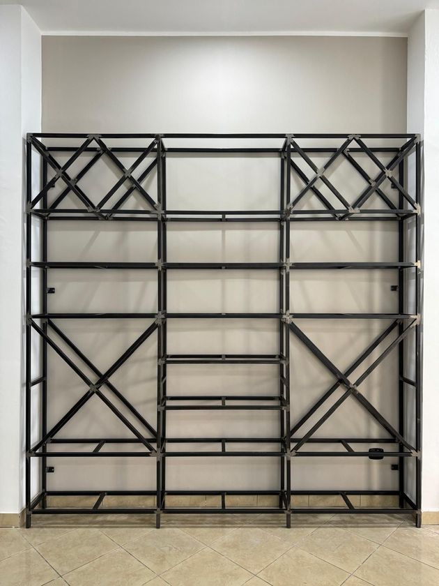 Scaffale in metallo nero contro una parete neutra. Design geometrico con ripiani di diverse dimensioni.