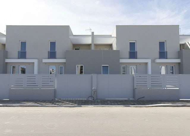 Case a schiera grigie dietro una recinzione coordinata, una giornata di sole.