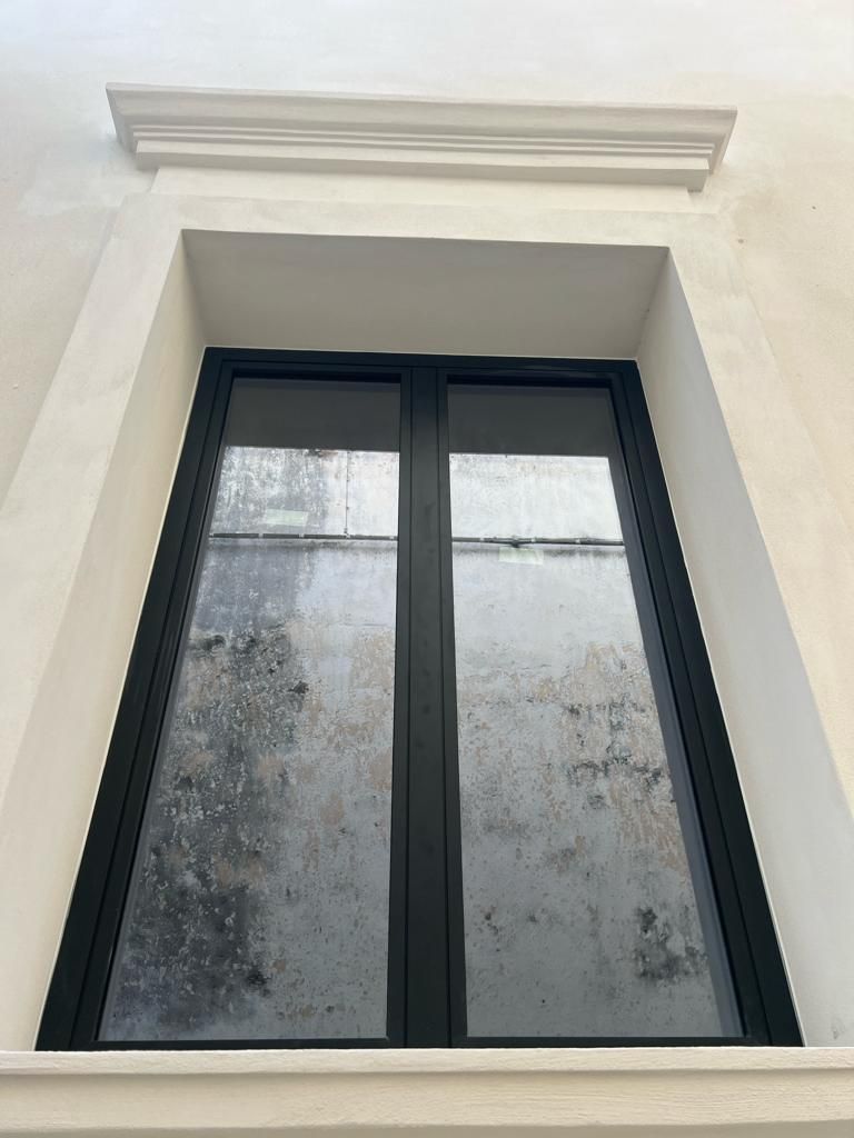 Finestra con cornice nera e vetro smerigliato, inserita in un edificio bianco. 