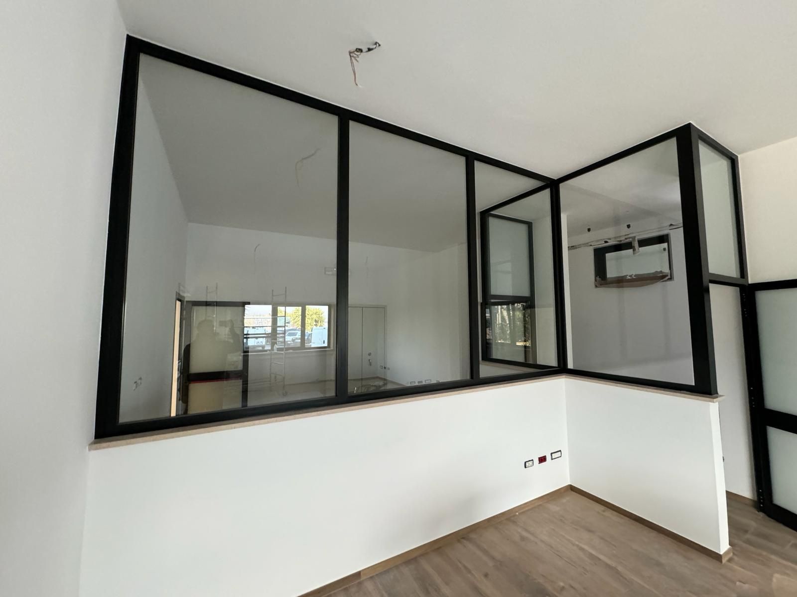 Interno con pareti in vetro con cornice nera e pareti bianche; pavimento in legno; 