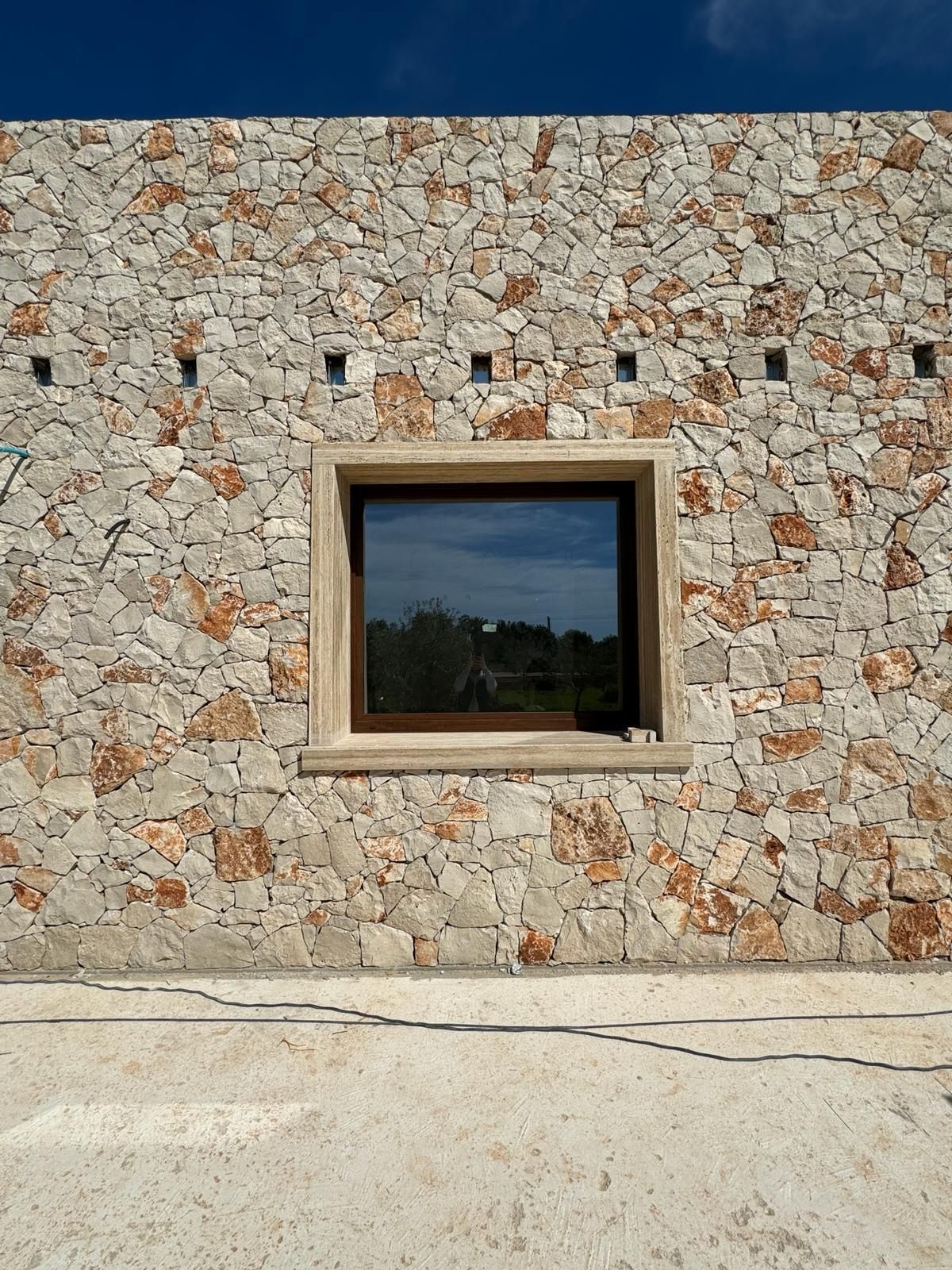 Muro di pietra con una finestra con cornice marrone e piccole aperture quadrate nella parte superiore