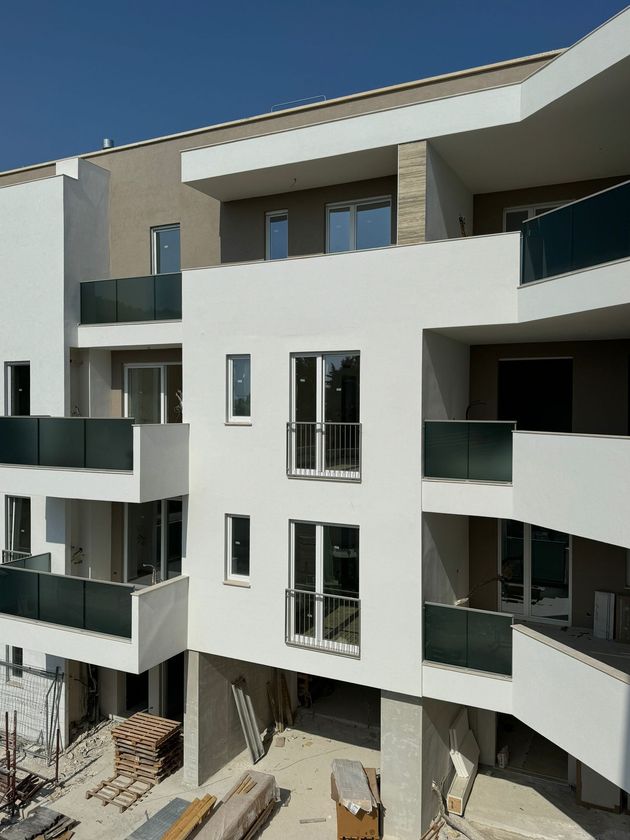Edificio residenziale a più piani in costruzione con facciata bianca e ringhiere dei balconi verde scuro.