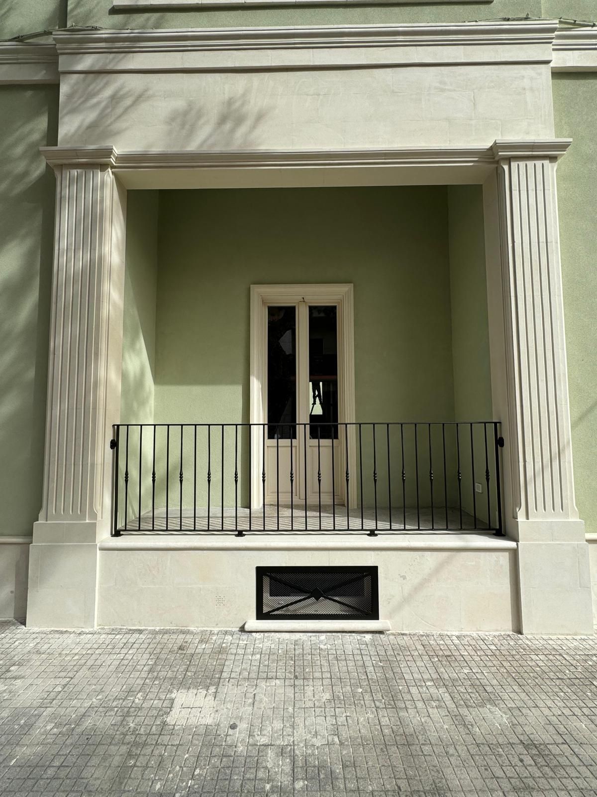 Facciata di un edificio verde e bianco con portale sostenuto da colonne e piccola ringhiera nera.