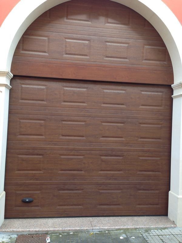 Porta da garage marrone con parte superiore arcuata, inserita in un portale con cornice bianca.