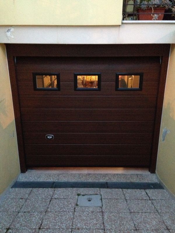 Portone da garage marrone con tre finestre. L'ambiente è un cortile.