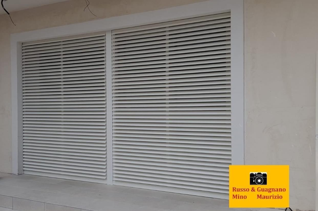 Persiane bianche a stecche inserite in una cornice su una parete esterna.