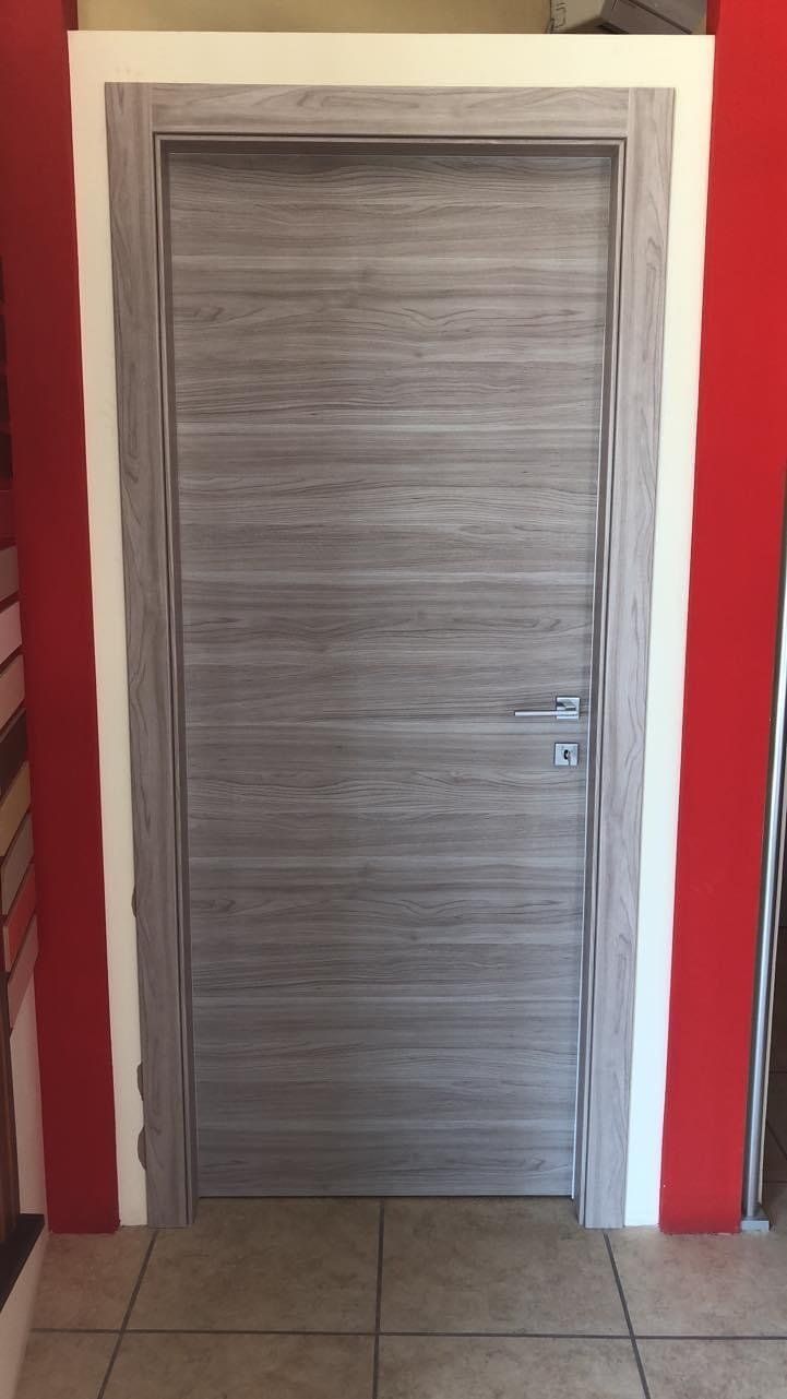 Porta in legno grigio con ferramenta argentata, incorniciata in bianco, incastonata in pareti rosse.