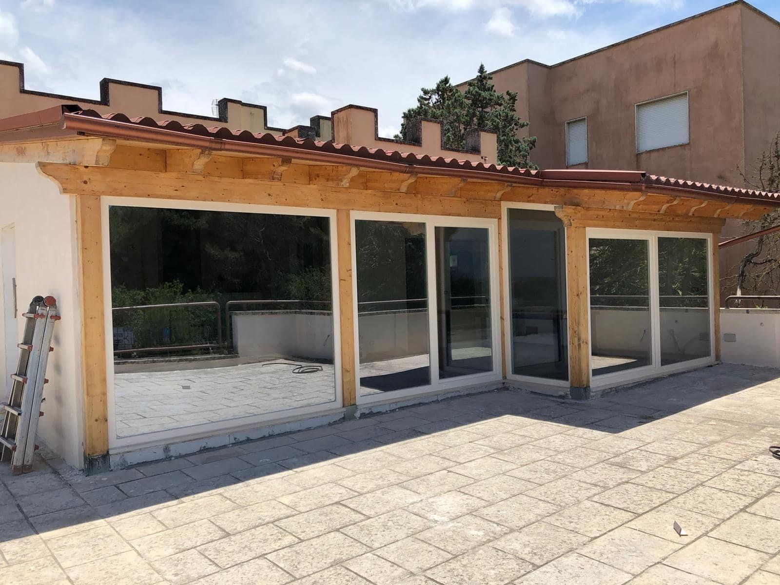 Struttura esterna con pareti in vetro e tetto in tegole rosse su un patio in pietra.