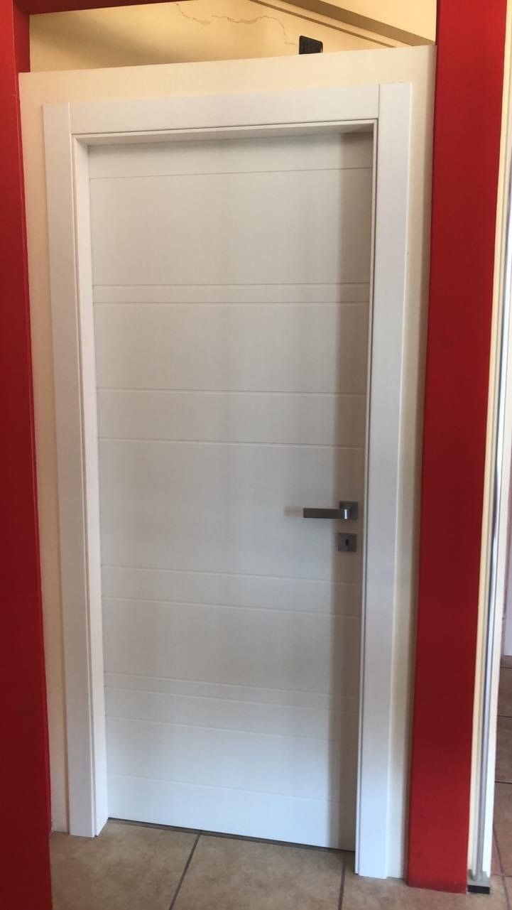 Porta bianca con scanalature orizzontali e maniglia argentata, incorniciata da finiture bianche su pareti rosse.