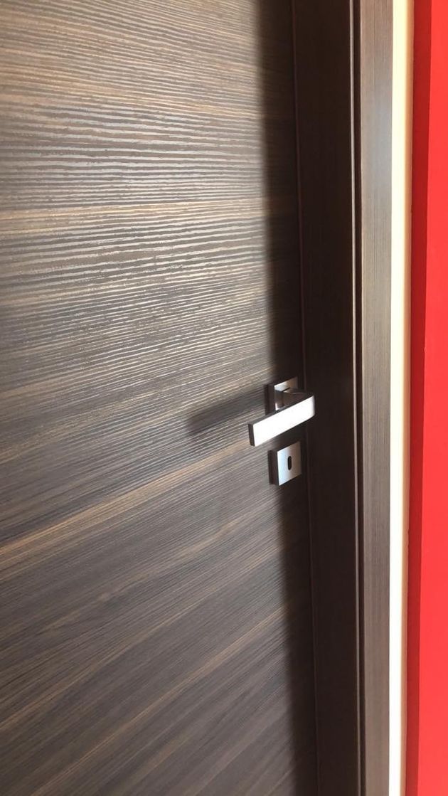 Porta in legno scuro con maniglia argentata; parete rossa sulla destra.
