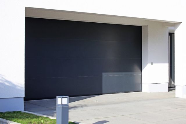 Porta da garage grigio scuro su una moderna casa bianca, con vialetto d'accesso che conduce ad essa.