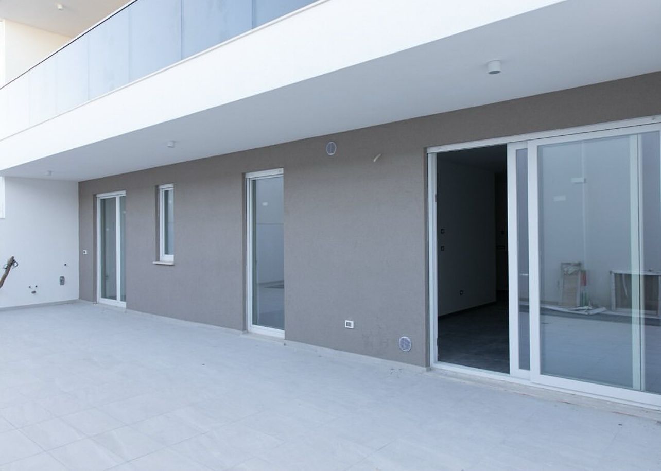 Esterno di un edificio moderno con pareti grigie, finestre bianche e una grande porta scorrevole in vetro.