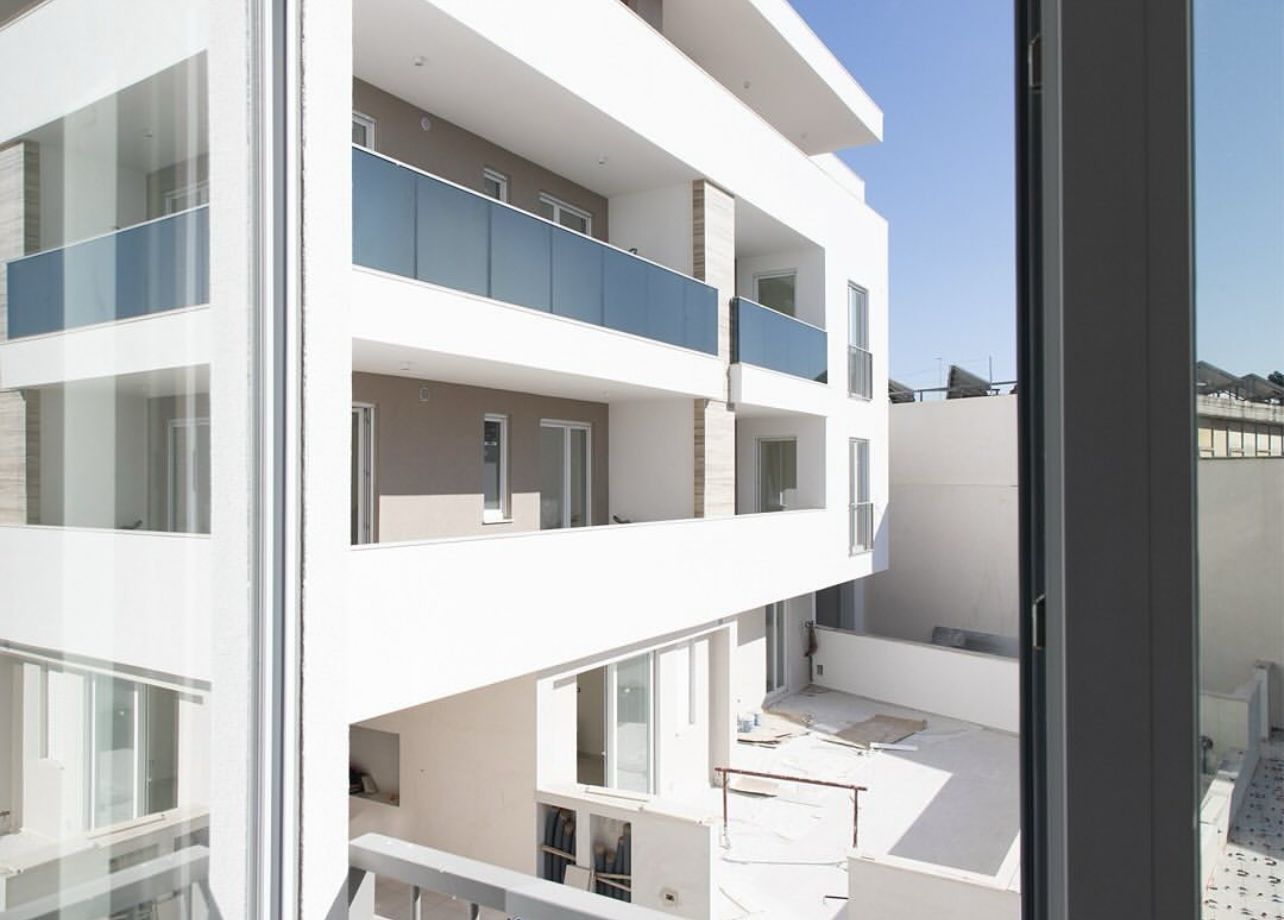 Moderno condominio bianco con balconi in vetro in una giornata di sole.