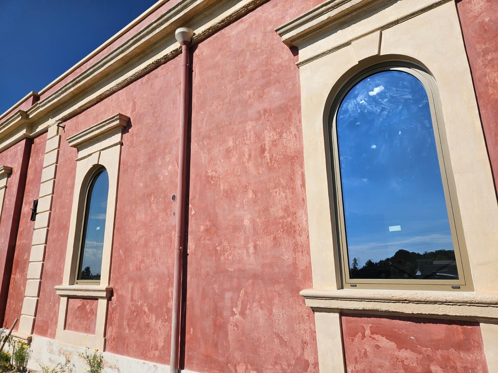 Edificio in stucco rosso con finestre ad arco, finiture beige, riflesso del cielo azzurro.