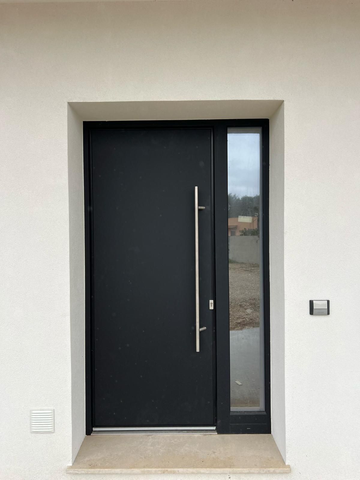 Porta d'ingresso nera con finestra laterale e lunga maniglia argentata.