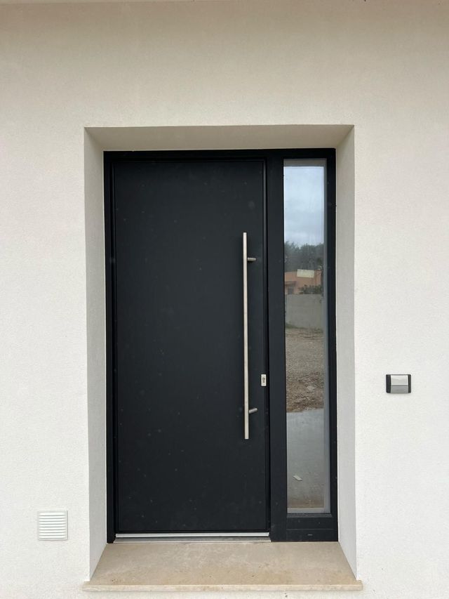 Porta d'ingresso nera con finestra laterale e lunga maniglia argentata.