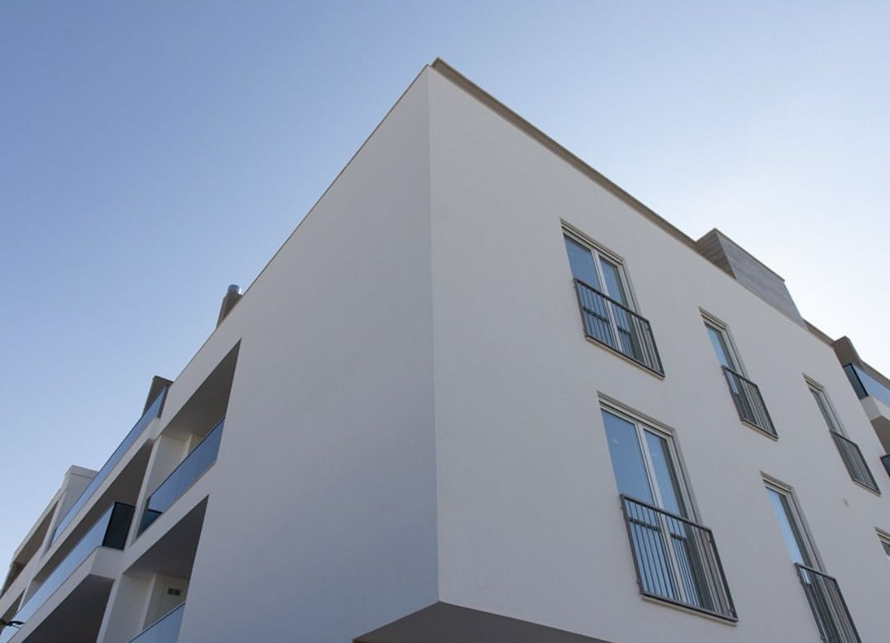 Angolo di un condominio bianco contro un cielo azzurro e terso. Balconi e finestre visibili.