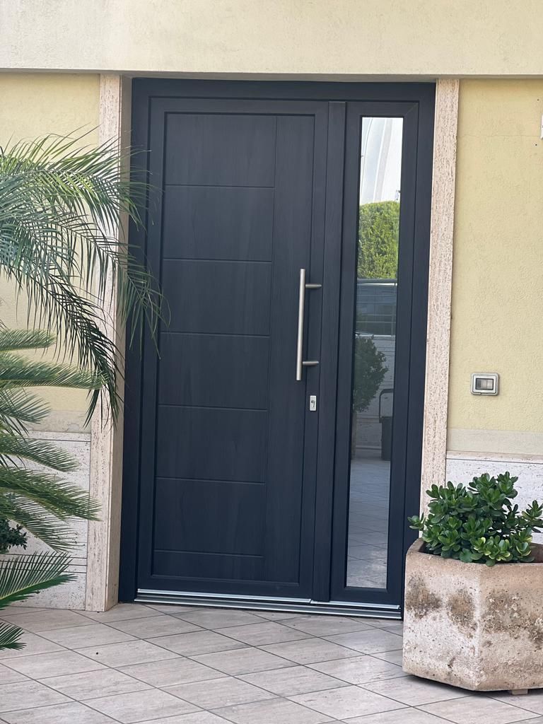 Porta nera con finestra laterale, piante in vaso e dettagli in pietra.