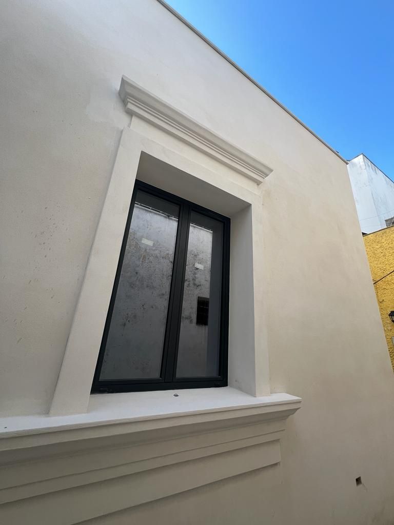 Finestra con rifiniture bianche su un edificio chiaro sotto un cielo azzurro.