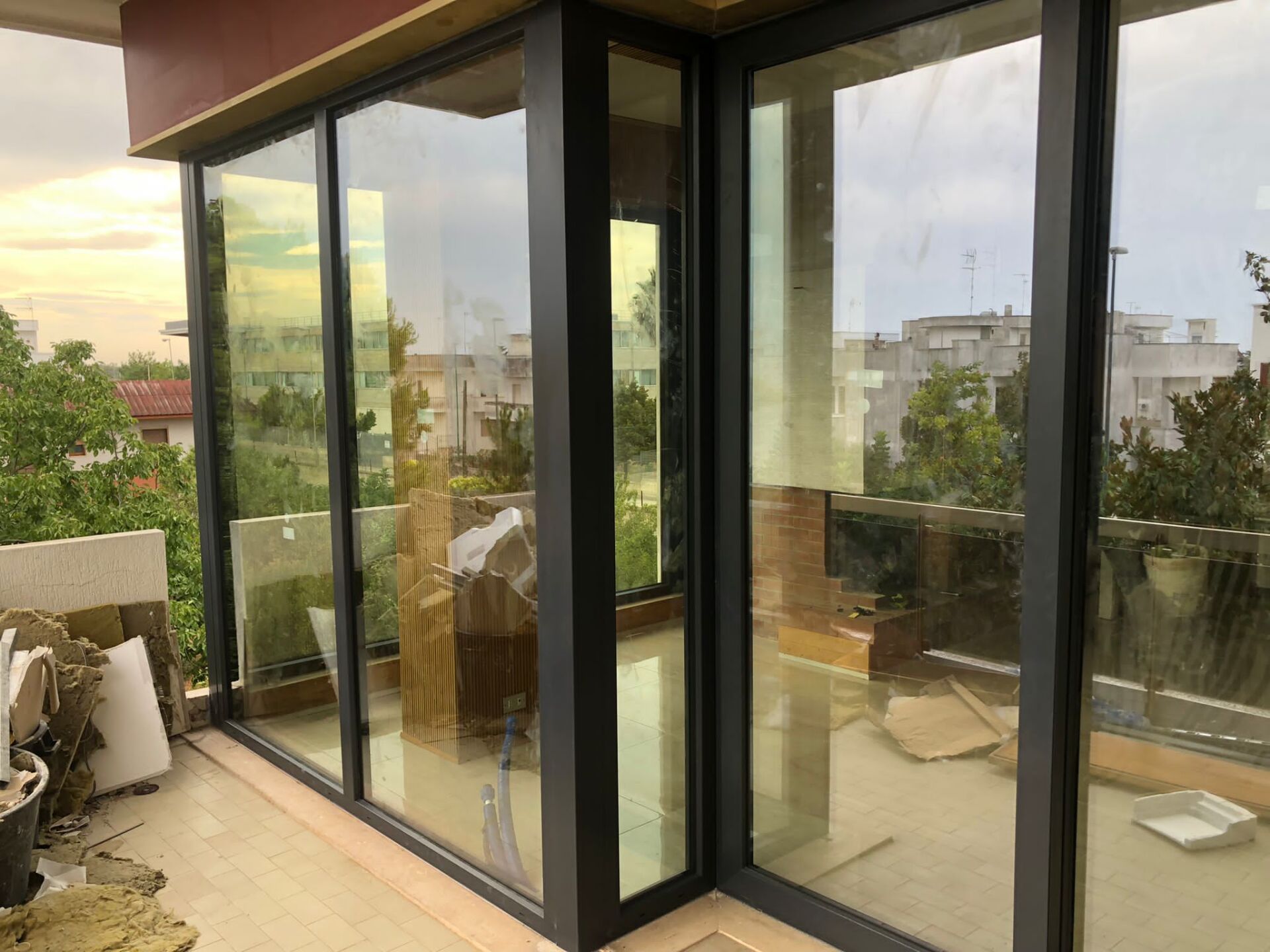 Porte scorrevoli in vetro con telai neri su un balcone che si affaccia su una zona residenziale alberata.