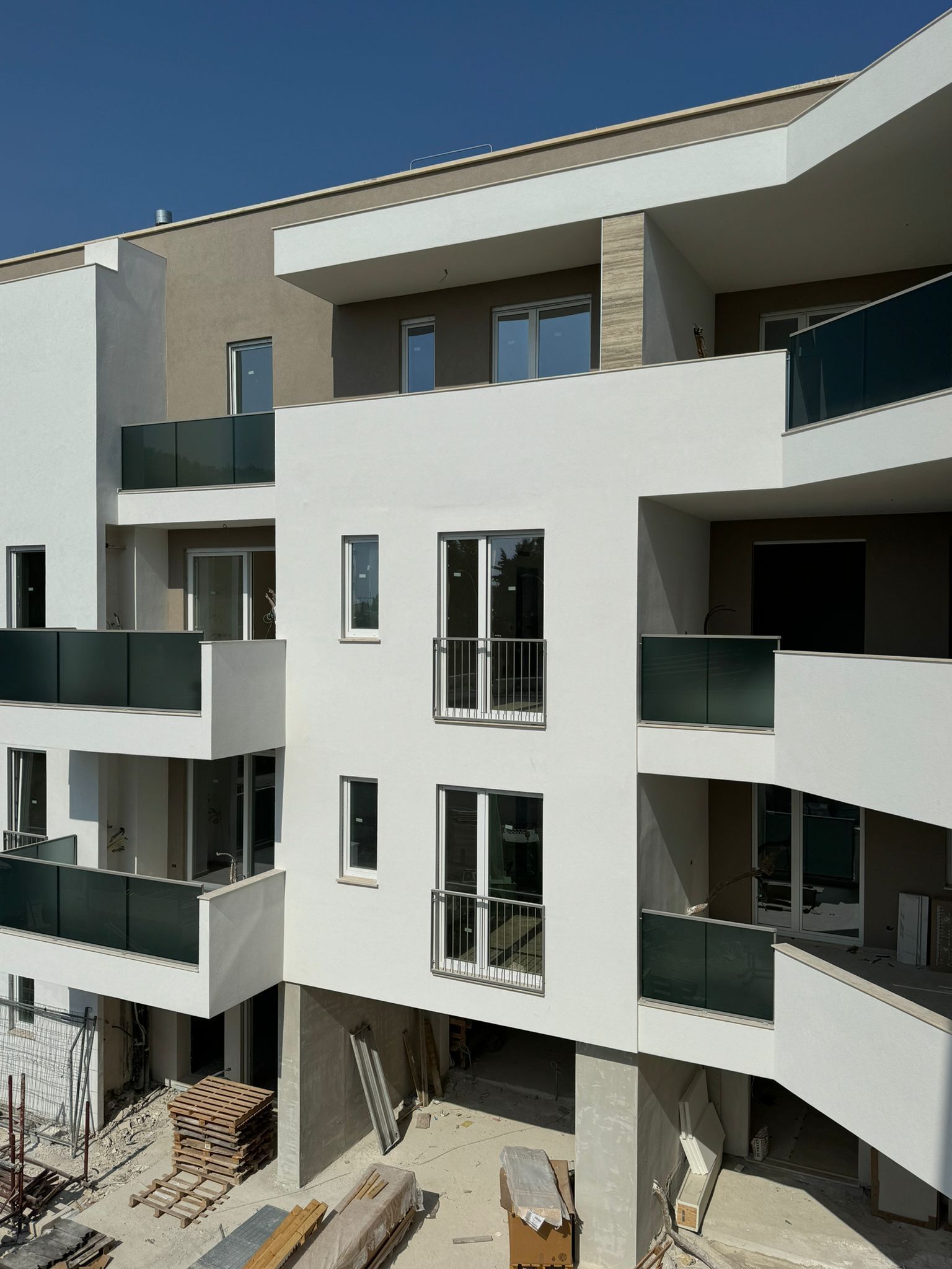Moderno condominio bianco con balconi; materiali da costruzione visibili sotto.