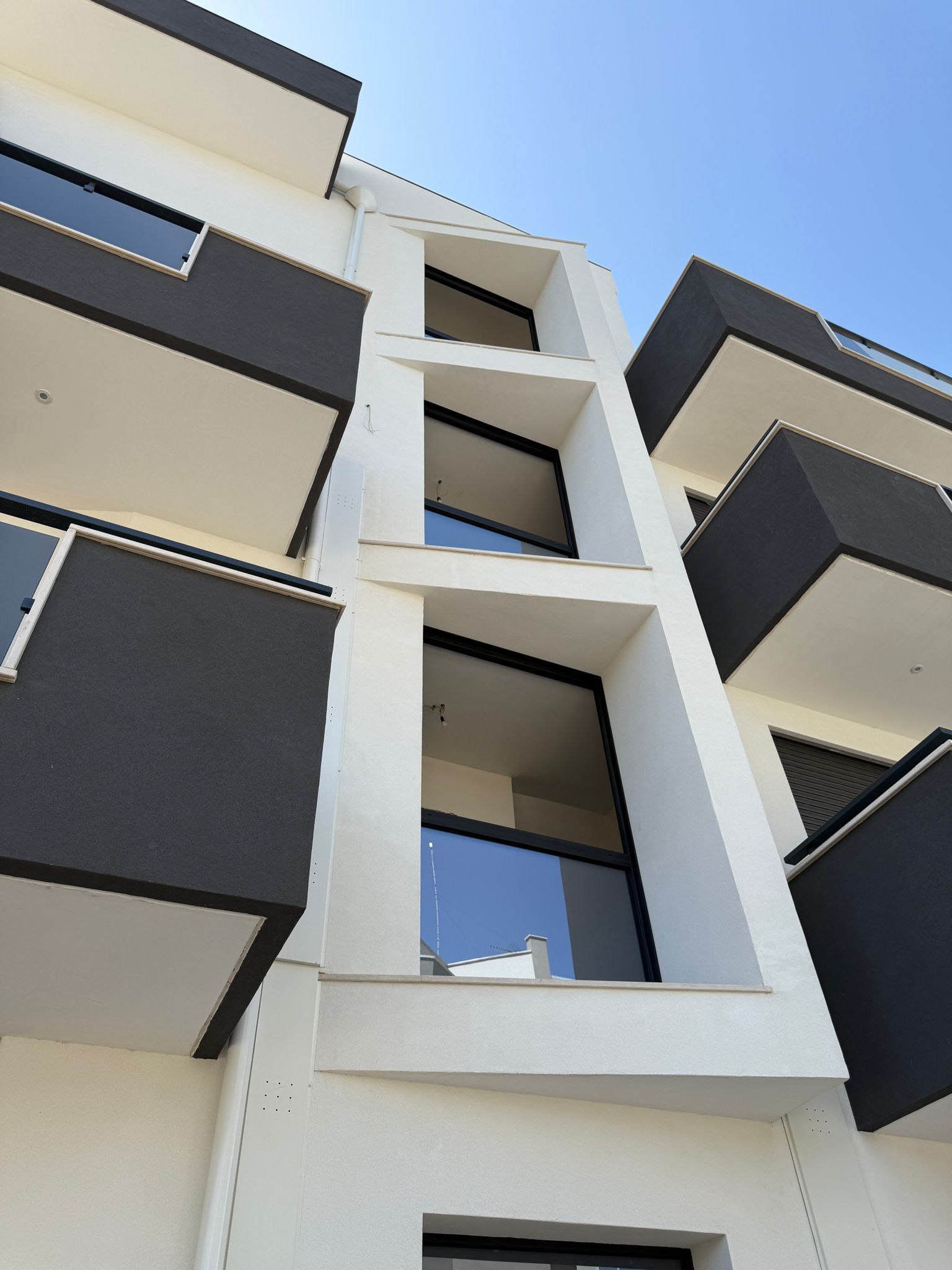 Edificio bianco con balconi scuri e grandi finestre contro il cielo azzurro.