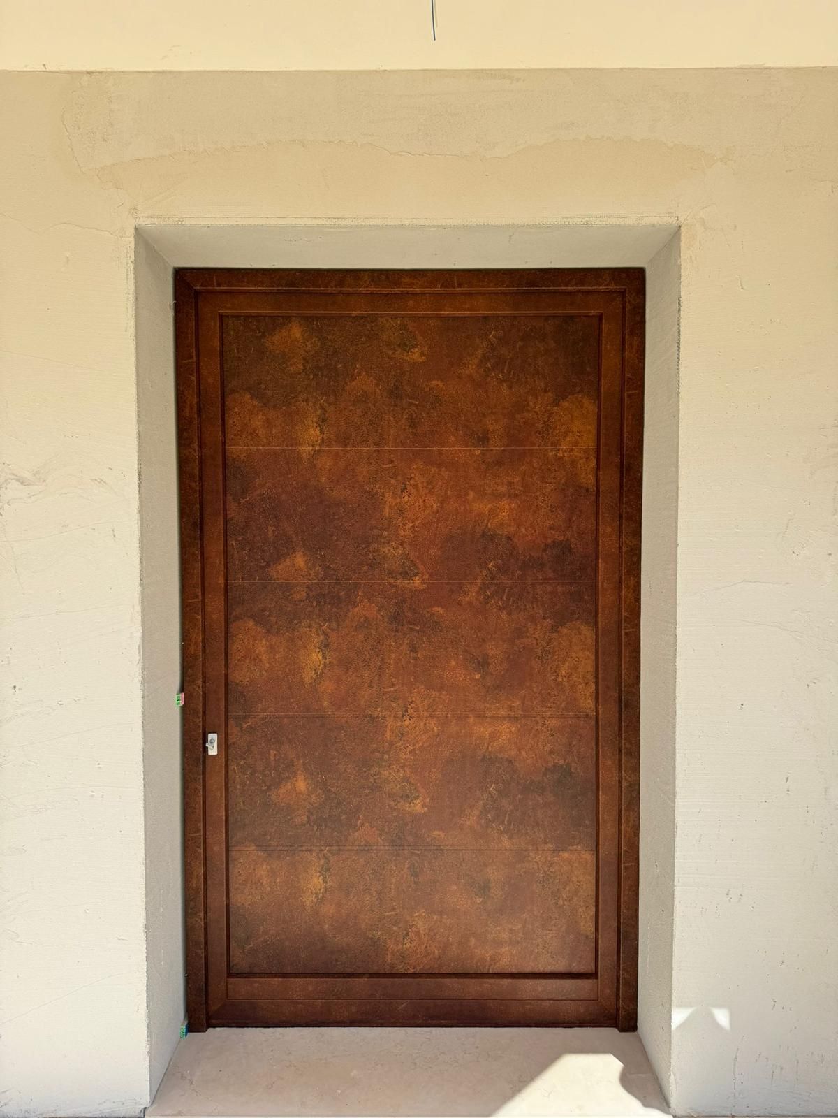 Una porta d'ingresso testurizzata color bronzo, inserita in un telaio bianco.