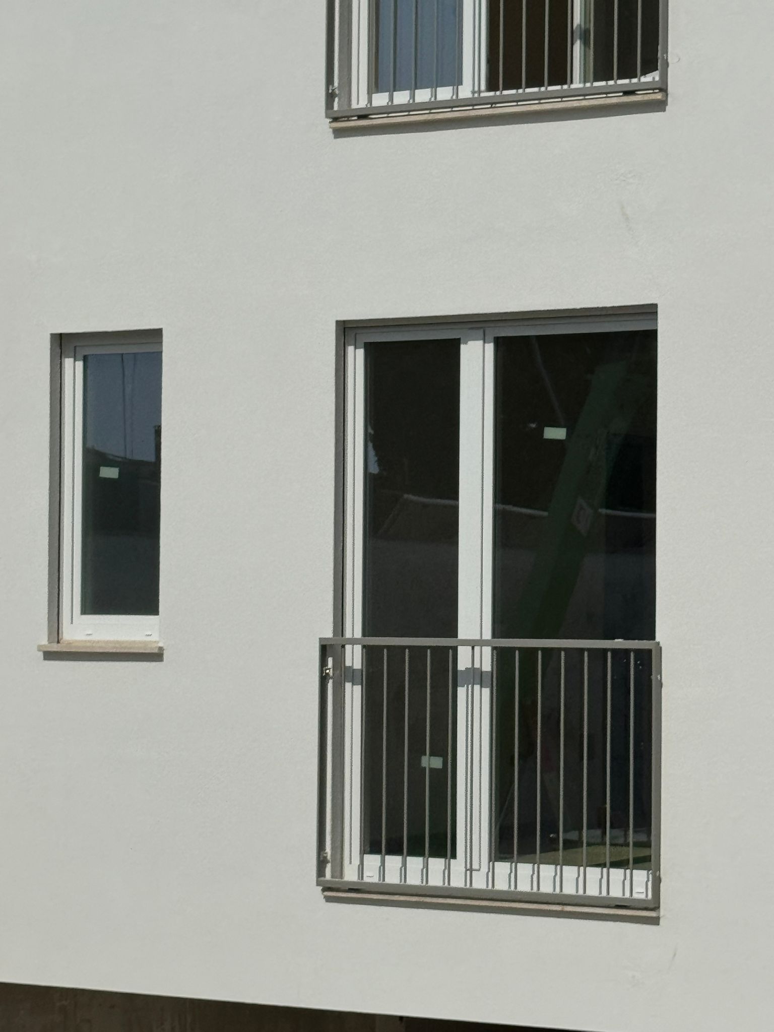 Facciata bianca dell'edificio con tre finestre: una stretta, una porta doppia e una finestra più piccola in alto.