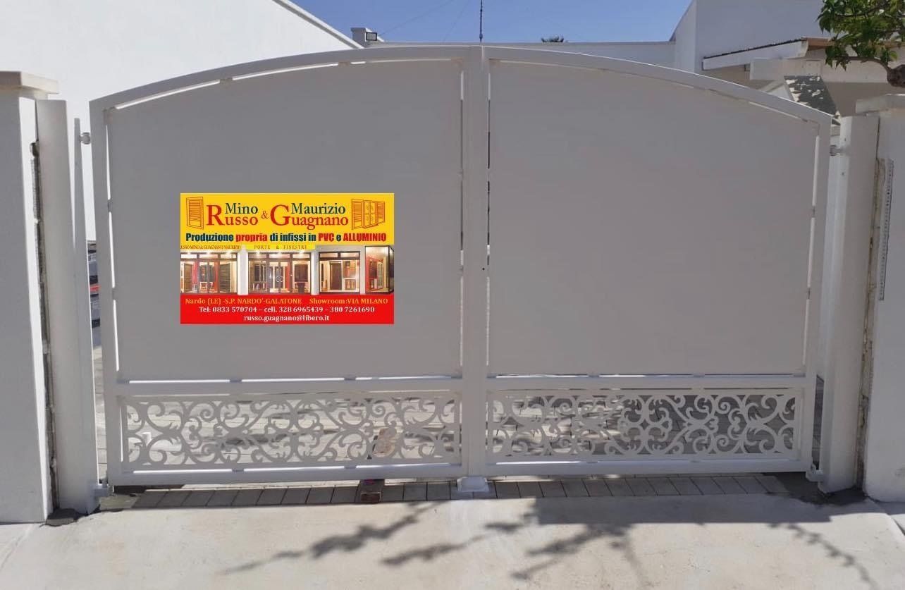 Cancello in metallo bianco con volute decorative e un cartello.