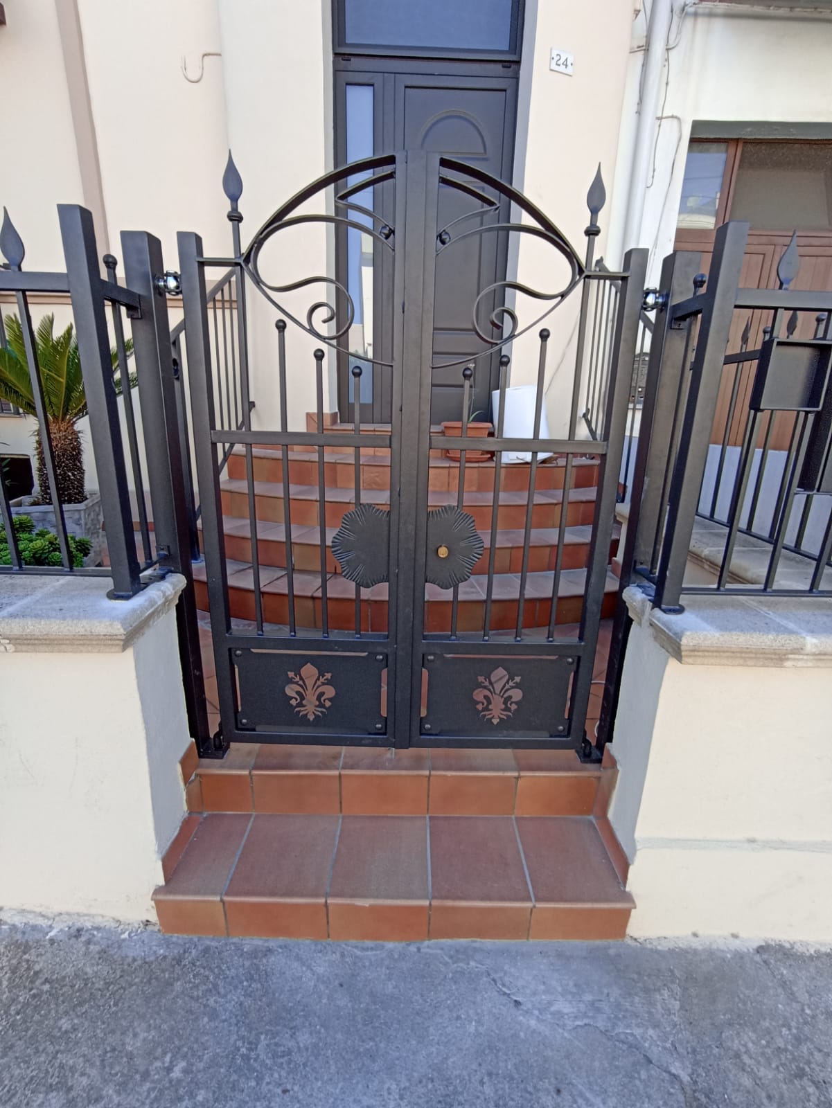 Cancello in metallo nero con motivo ornamentale, che conduce alla porta d'ingresso tramite piccoli gradini.