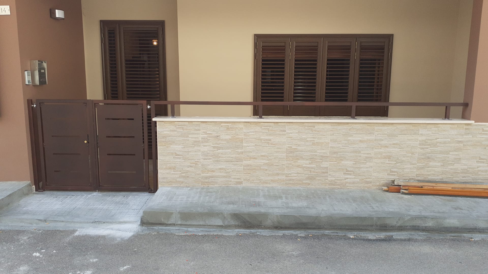 Cancello e finestre in metallo marrone su un edificio beige con facciata in pietra, poggiato su fondamenta di cemento.
