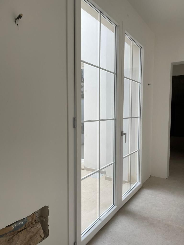 Porte finestre bianche con vetri a griglia, inserite in una stanza appena tinteggiata, che offrono una vista sull'esterno.