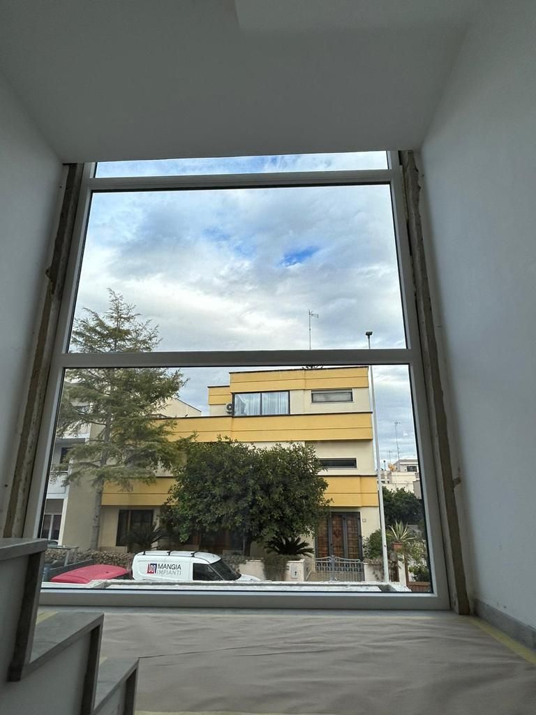 Vista attraverso una grande finestra di un edificio giallo e di un cielo nuvoloso; interno con scale incompiute.