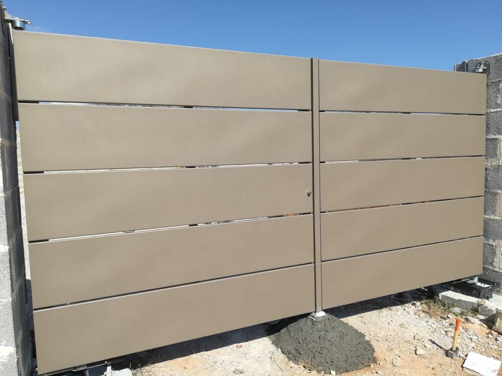 Cancello d'accesso in metallo color cuoio con listelli orizzontali tra pilastri in mattoni grigi