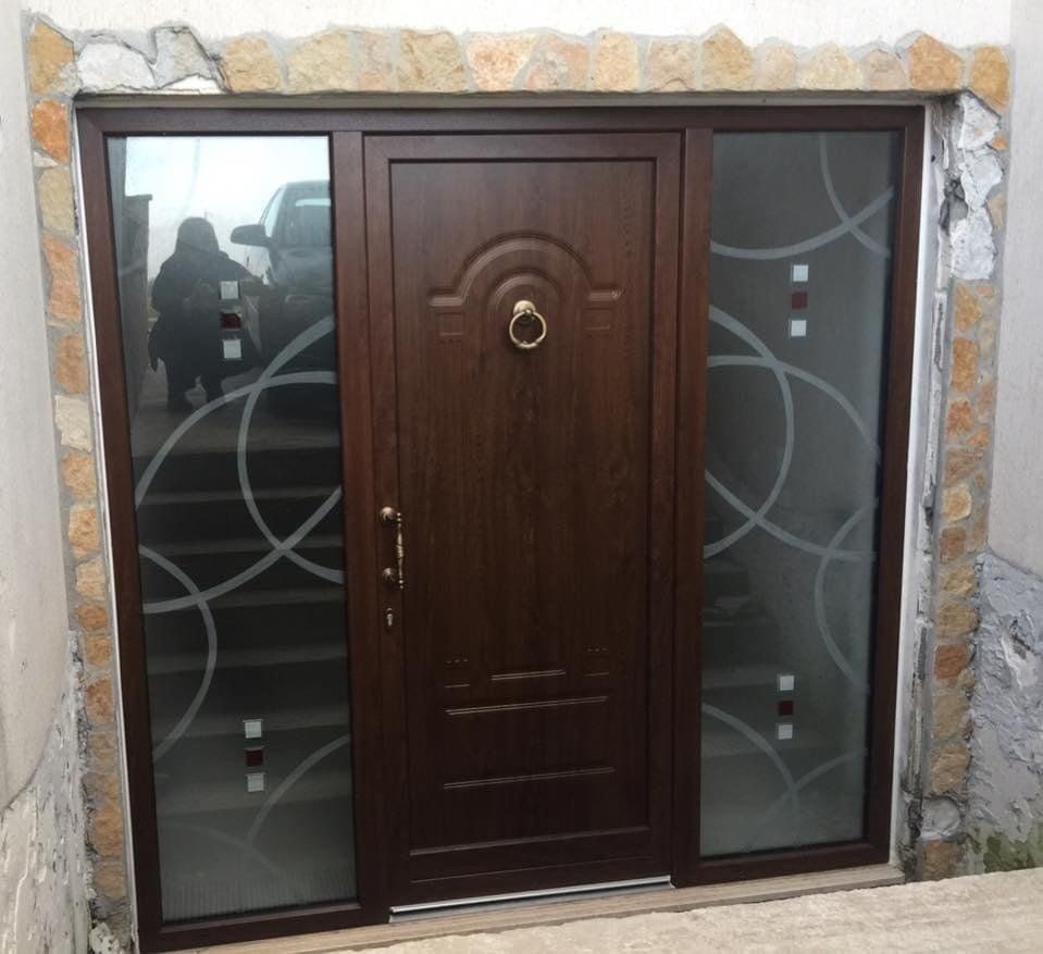 Porta d'ingresso marrone con vetri laterali, caratterizzata da un design in vetro smerigliato e cornice in pietra.