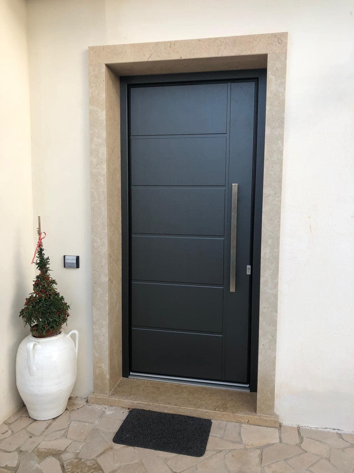 Porta d'ingresso grigio scuro con maniglia verticale, incastonata in una cornice di pietra