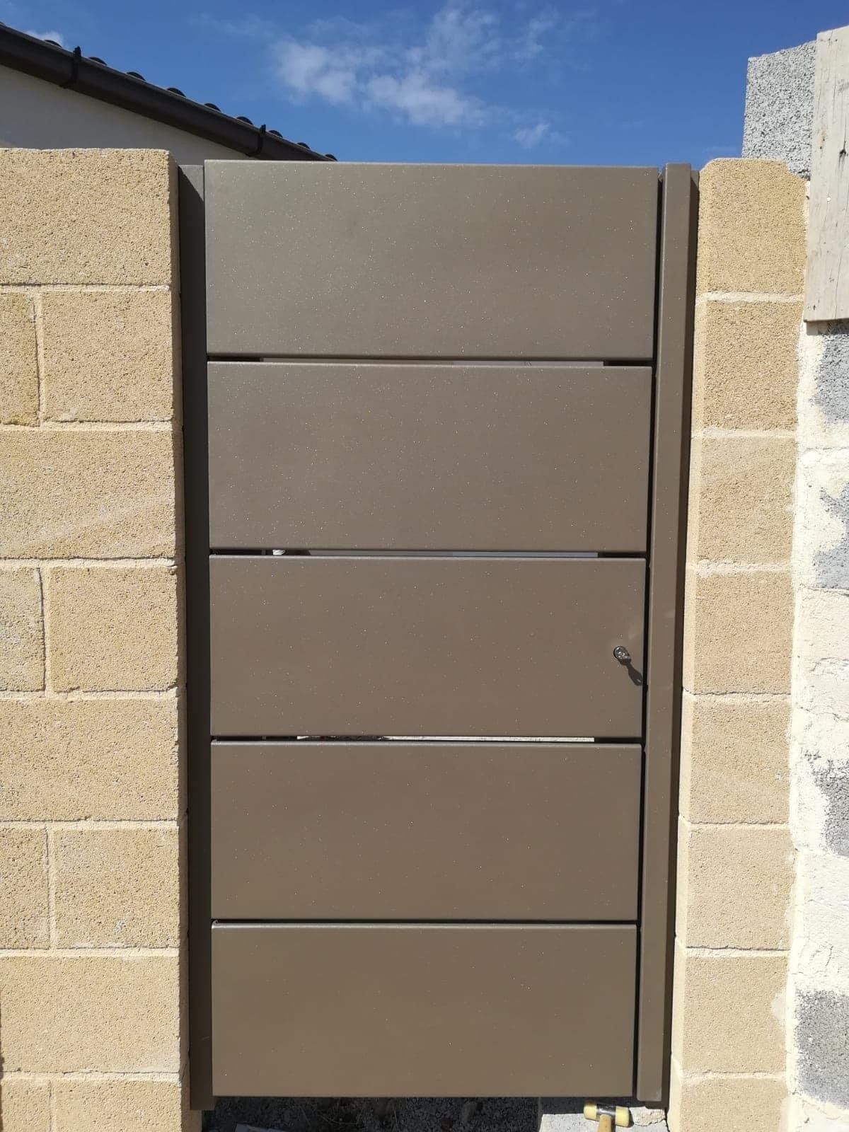 Cancello di metallo marrone su pilastri di mattoni, contro un cielo azzurro.